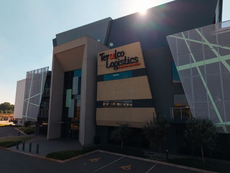Modern industrial logistics facility featuring contemporary metal cladding, decorative mesh screens, and a prominent glass-fronted entrance with dedicated parking.