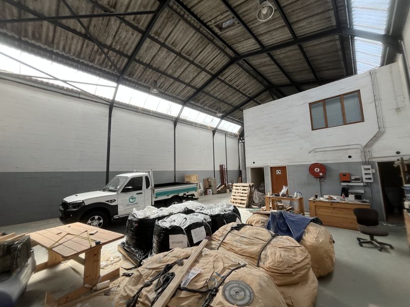Spacious industrial warehouse unit featuring high ceilings with exposed steel trusses, natural skylight illumination, concrete flooring, and integrated fire safety equipment.