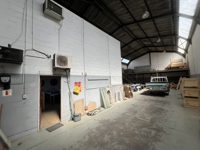 Spacious industrial utility area featuring high ceilings with exposed steel trusses, concrete flooring, and a mezzanine level suitable for storage or workspace.