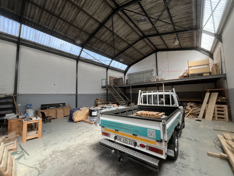 Spacious industrial utility area featuring a mezzanine level, steel staircase, high ceilings with translucent roof panels, and durable concrete flooring.