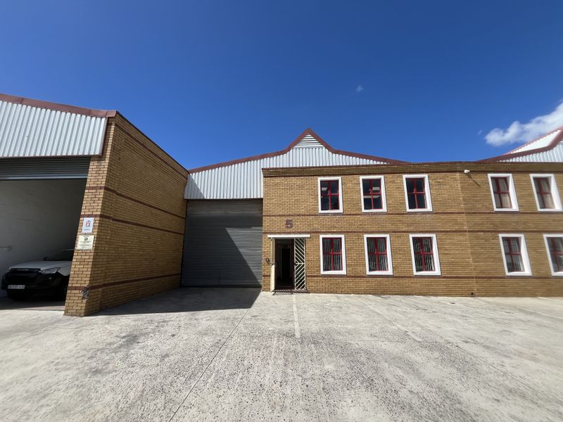 Front elevation of an industrial warehouse unit featuring face brick construction, roller shutter access, and secure window treatments with a concrete forecourt.