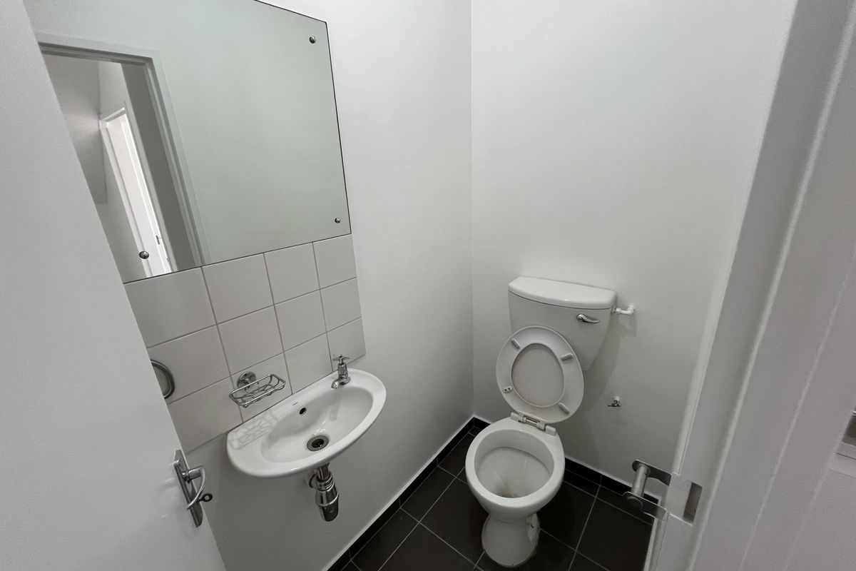 A clean, functional guest bathroom featuring a wall-mounted basin, toilet, and tiled flooring in a neutral, well-maintained space.
