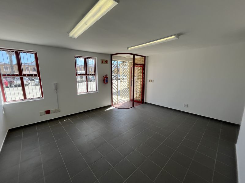 A clean, empty office space featuring tiled flooring, fluorescent lighting, security bars on windows, and a secure entrance gate.