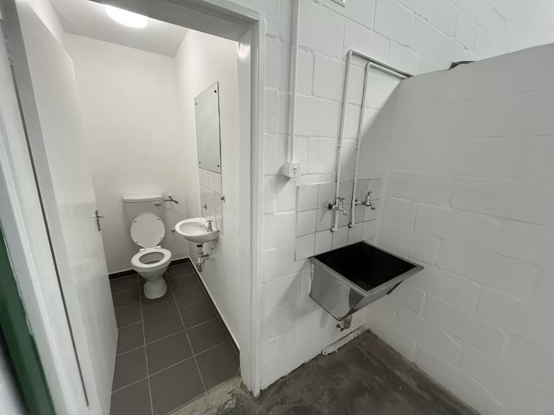 Industrial utility area featuring a stainless steel sink, exposed blockwork walls, and an adjacent private restroom with a toilet and basin.