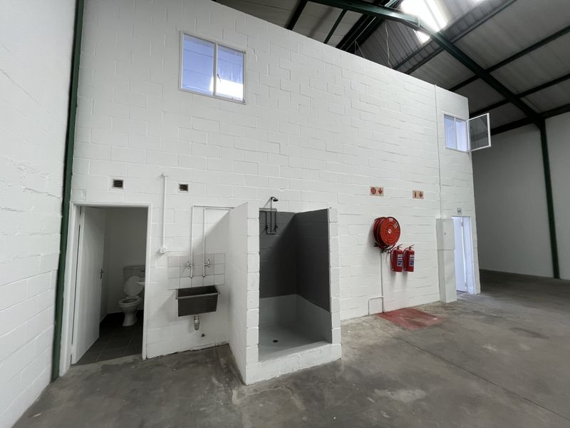 Industrial utility space featuring concrete flooring, exposed roof trusses, a built-in shower, utility sink, and essential fire safety equipment.