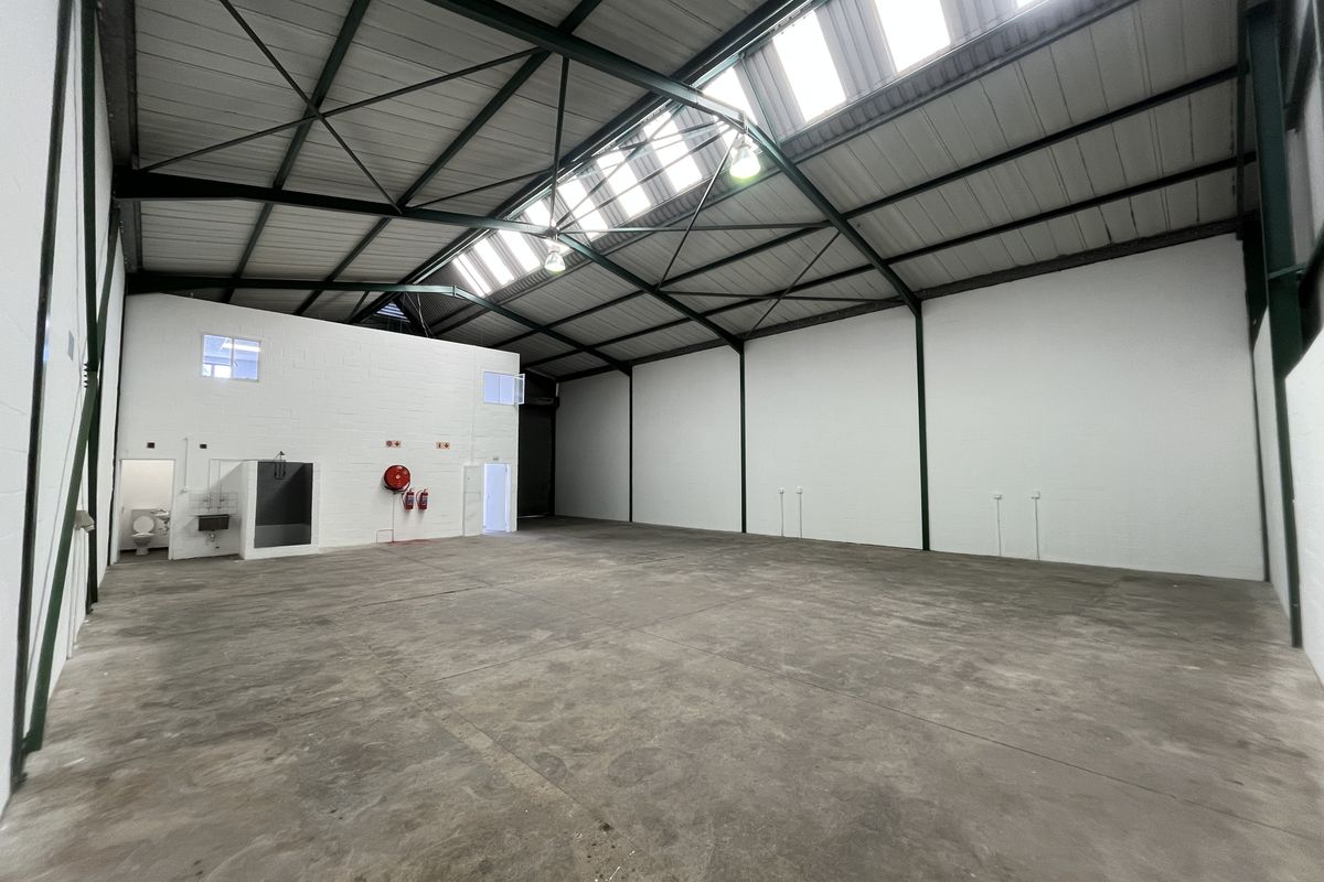 Spacious industrial warehouse unit featuring high ceilings with skylights, concrete flooring, and integrated ablution facilities, suitable for various commercial or storage operations.
