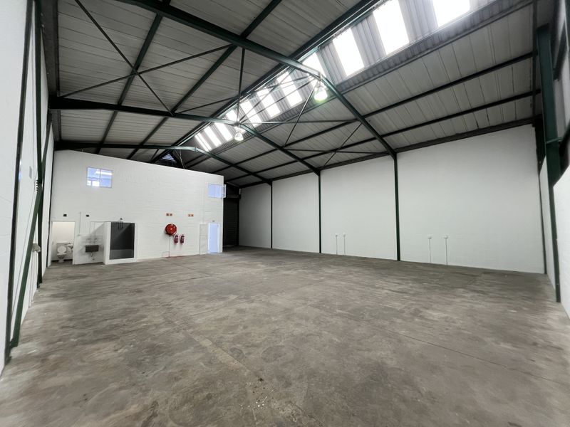 Spacious industrial warehouse unit featuring high ceilings with skylights, concrete flooring, and integrated ablution facilities, suitable for various commercial or storage operations.