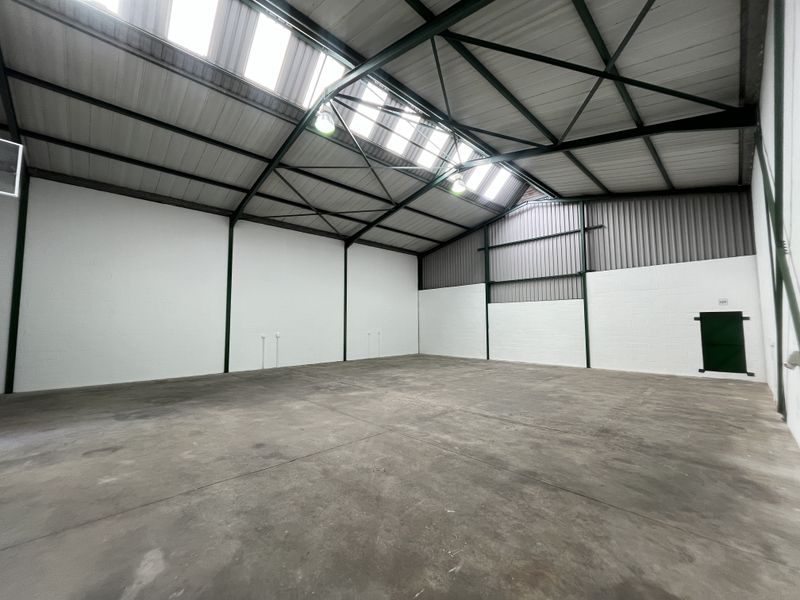 Spacious industrial warehouse unit featuring high ceilings with exposed steel trusses, integrated skylights, concrete flooring, and clean painted blockwork walls.