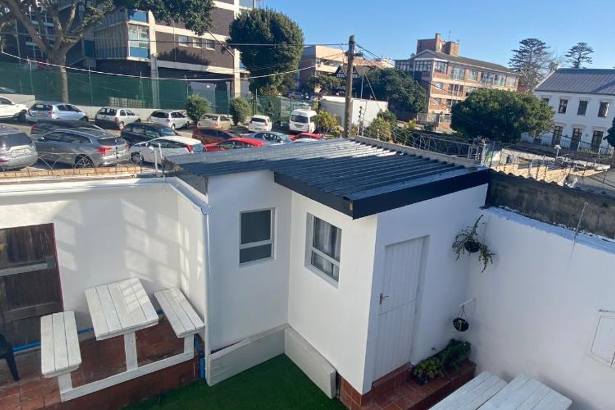 A rear courtyard area featuring artificial grass, terracotta tiling, and a small outbuilding with a corrugated metal roof.