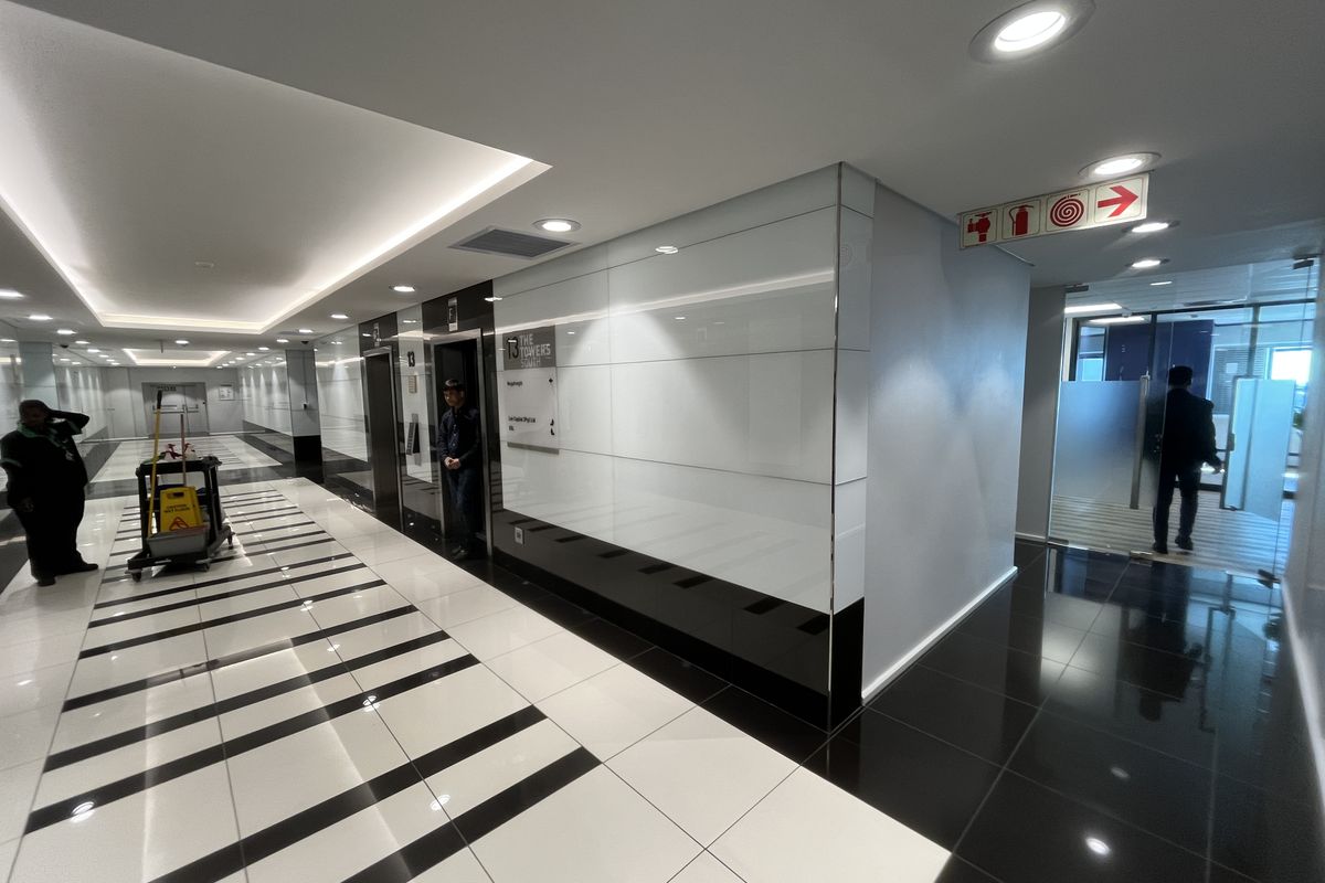 Modern office building hallway featuring high-gloss tiled flooring, recessed ceiling lighting, and professional elevator access with glass partition detailing.