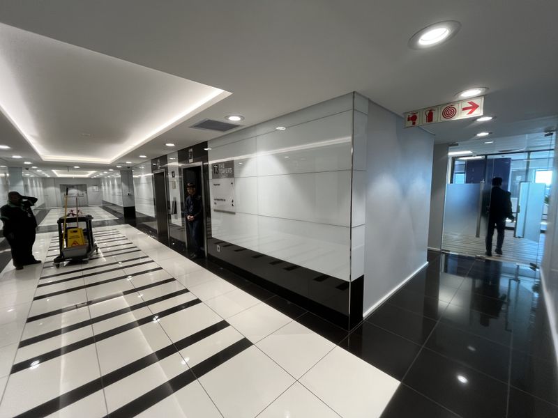 Modern office building hallway featuring high-gloss tiled flooring, recessed ceiling lighting, and professional elevator access with glass partition detailing.