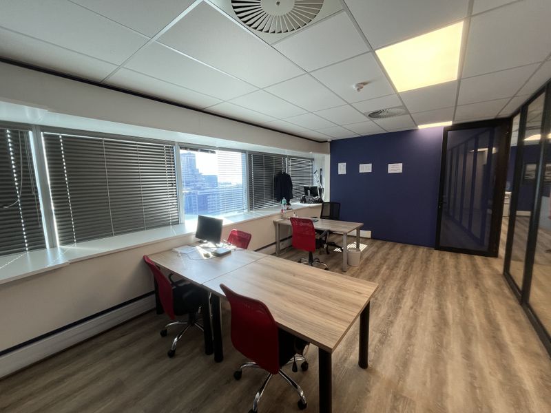 Modern office space featuring laminate flooring, suspended ceiling with recessed lighting, and large windows with venetian blinds, offering a professional work environment.