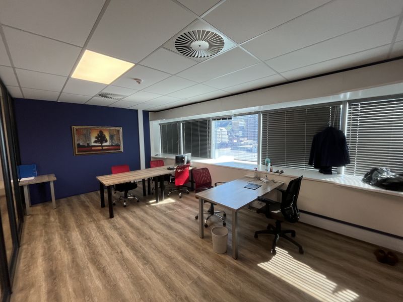 A bright, modern office space featuring laminate flooring, suspended ceilings with integrated lighting, and large windows with venetian blinds offering natural light.
