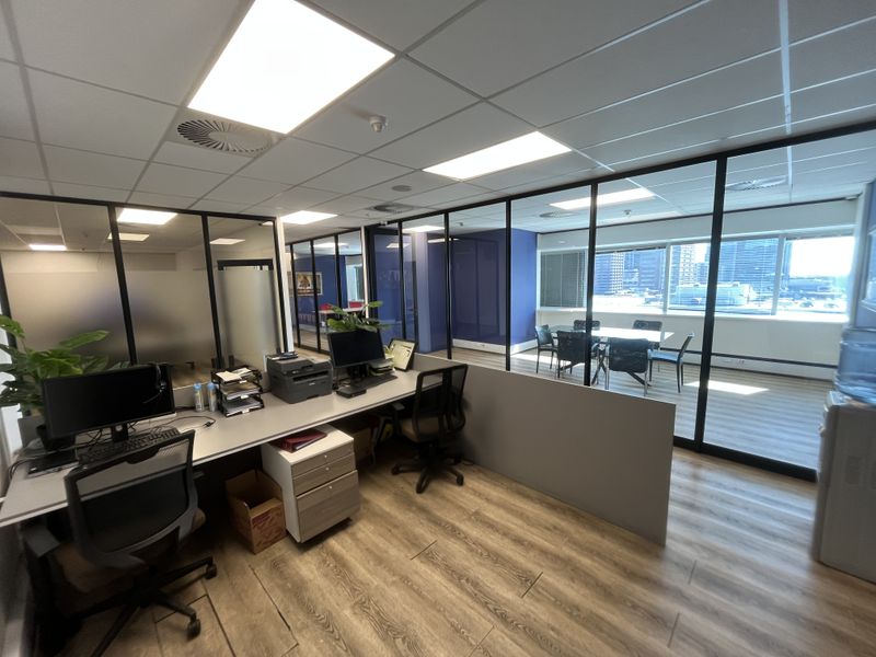 Modern office space featuring glass partition walls, suspended ceilings with recessed lighting, and durable laminate flooring, providing a professional and open work environment.