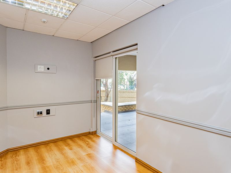A bright, empty office space featuring laminate flooring, a suspended ceiling with recessed lighting, and a sliding glass door leading to an outdoor area.