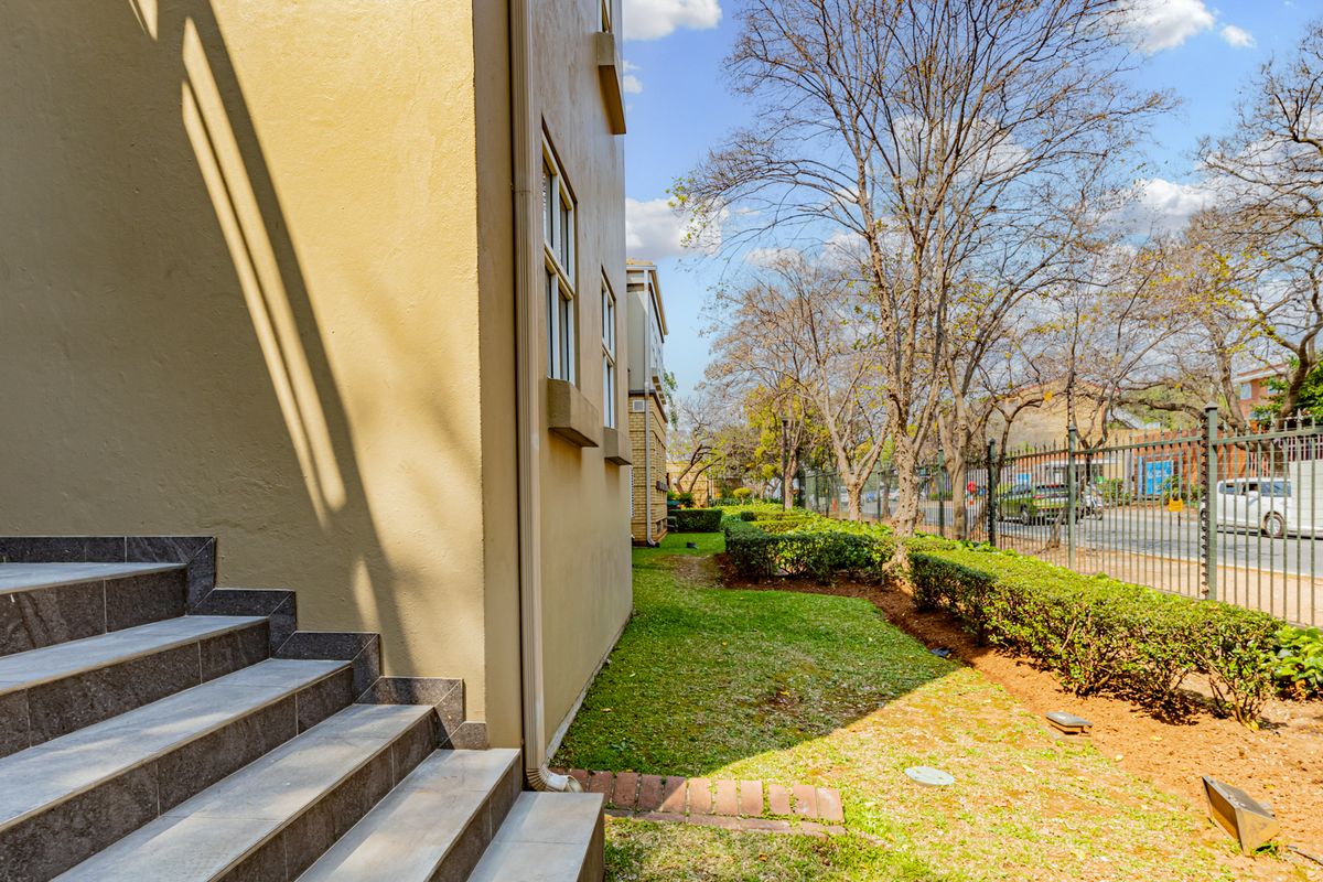 A side view of the office building featuring a tiled staircase, landscaped garden area, and secure metal perimeter fencing along the street boundary.