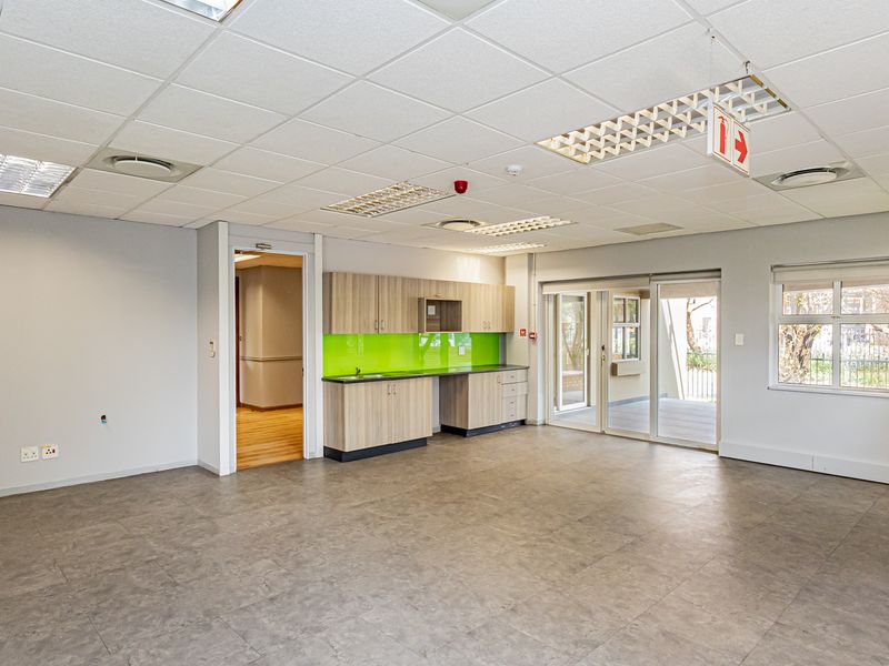 Spacious open-plan office area featuring a modern kitchenette, durable flooring, suspended ceilings with recessed lighting, and direct access to an outdoor patio.