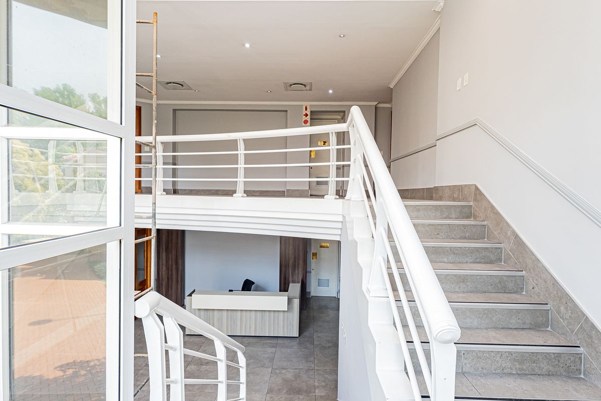 Spacious office entrance featuring a central staircase with white railings, tiled flooring, and recessed lighting, providing a bright and professional reception area.