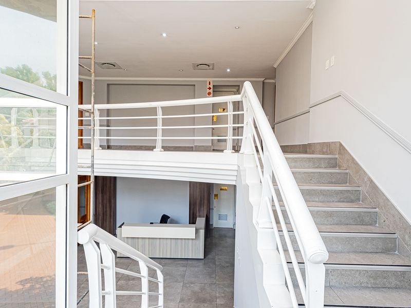 Spacious office entrance featuring a central staircase with white railings, tiled flooring, and recessed lighting, providing a bright and professional reception area.