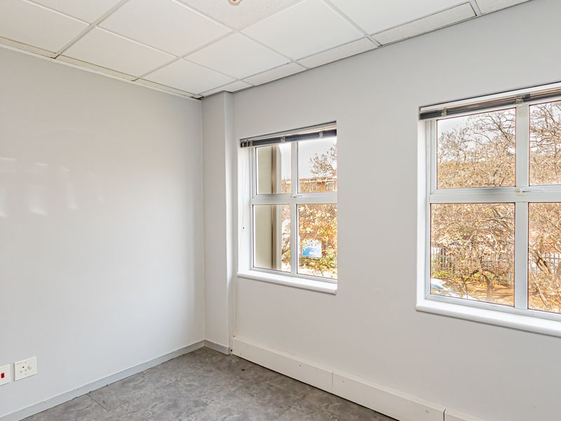 A bright, empty office space featuring a suspended ceiling, neutral walls, and large windows with venetian blinds, providing ample natural light.