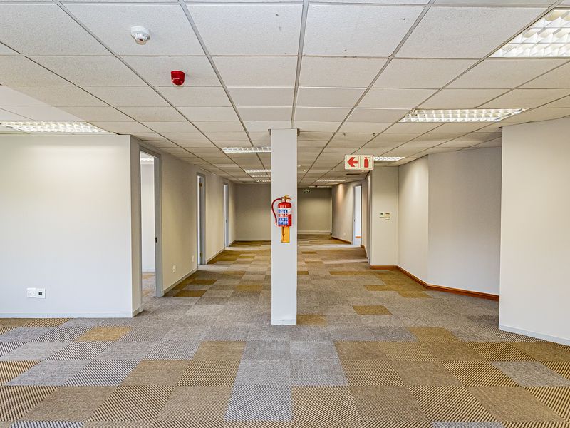 An open-plan office space featuring a suspended ceiling with recessed lighting, carpet tile flooring, and central structural support column.