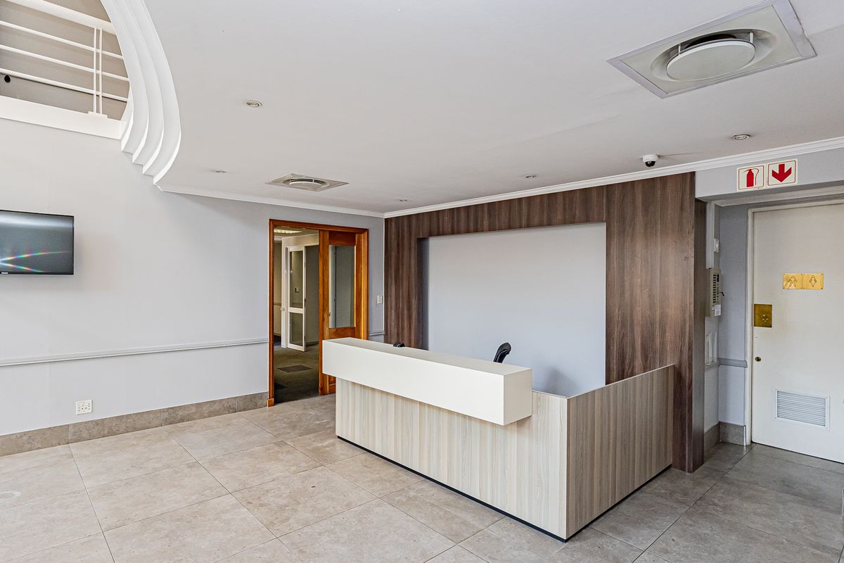 A professional office reception area featuring a modern built-in desk, tiled flooring, recessed lighting, and clean neutral finishes.