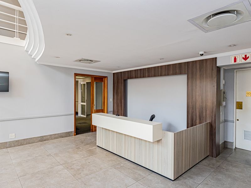 A professional office reception area featuring a modern built-in desk, tiled flooring, recessed lighting, and clean neutral finishes.
