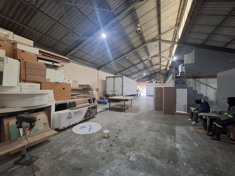 Spacious industrial warehouse unit featuring high exposed steel roof trusses, concrete flooring, and a mezzanine level suitable for storage or workshop operations.