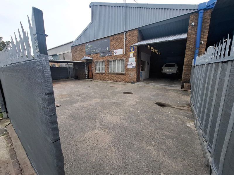Industrial property exterior featuring a brick facade, corrugated metal roofing, secure perimeter fencing, and a large roller shutter door for vehicle access.