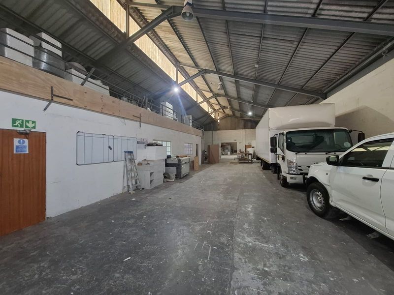 Spacious industrial warehouse unit featuring high ceilings with exposed steel trusses, concrete flooring, and a mezzanine level suitable for storage or office conversion.