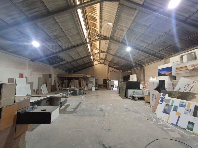 Spacious industrial warehouse featuring high exposed steel roof trusses, corrugated metal roofing, and durable concrete flooring, suitable for various manufacturing or storage operations.