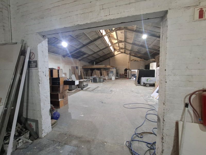 Spacious industrial utility area featuring exposed timber roof trusses, concrete flooring, and painted brick walls, suitable for workshop or storage use.