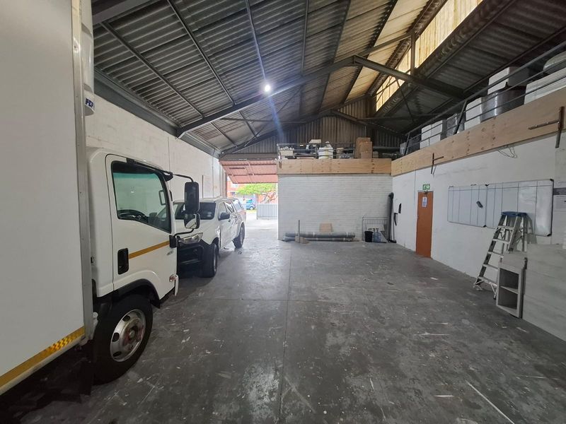 Spacious industrial garage featuring high exposed steel roof trusses, concrete flooring, and a mezzanine storage level, suitable for vehicle storage or workshop use.