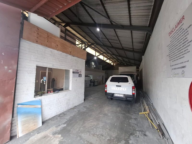 Spacious industrial warehouse or garage area featuring exposed steel roof trusses, concrete flooring, and an integrated internal office partition.