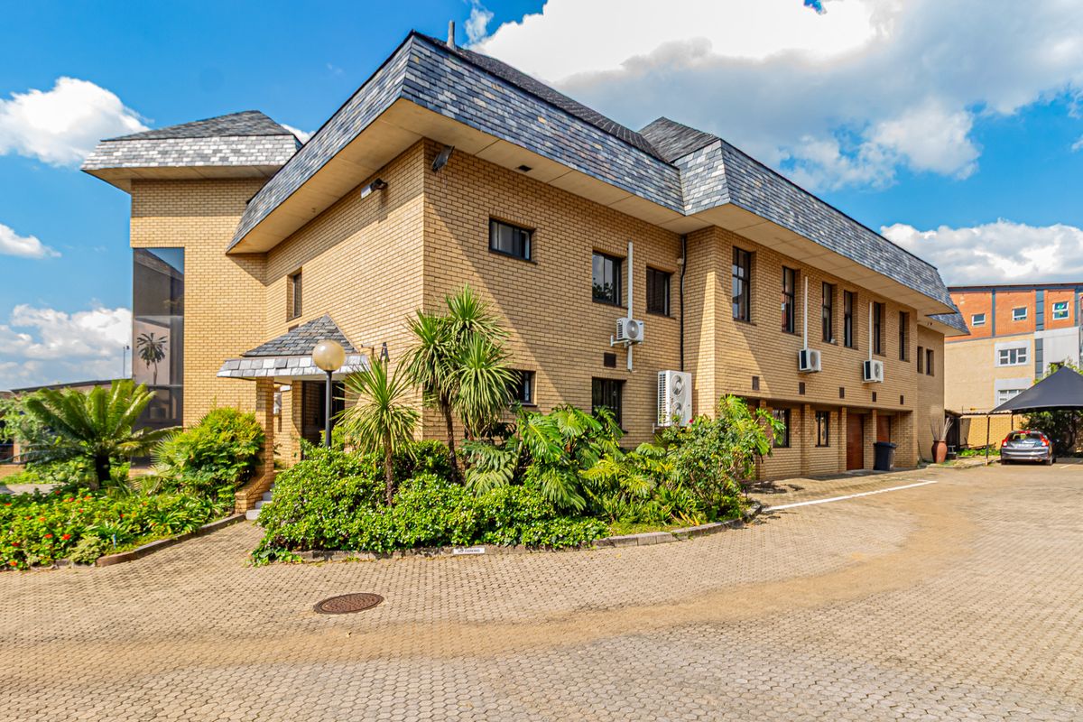 A well-maintained multi-story office building featuring a classic brick facade, slate roofing, and a paved driveway with established garden landscaping.