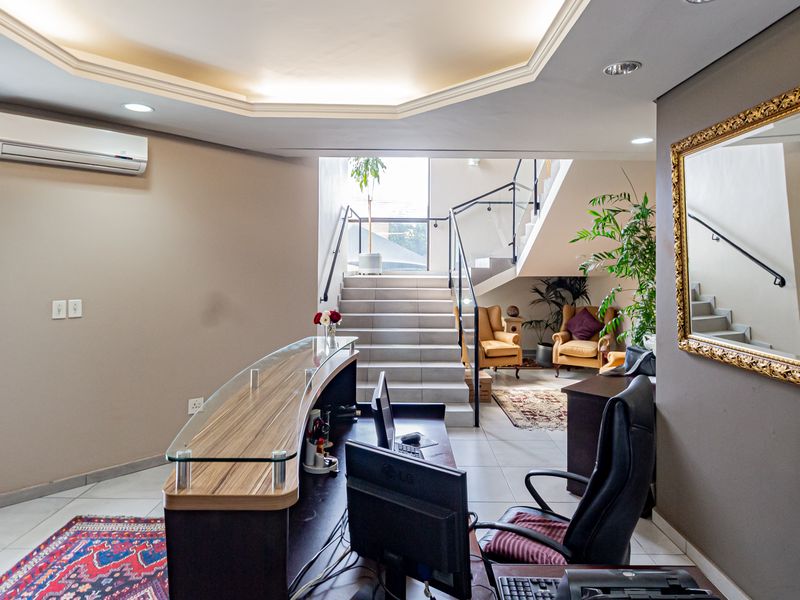 Professional office reception area featuring a modern glass-topped desk, tiled flooring, recessed lighting, and a staircase leading to the upper level.
