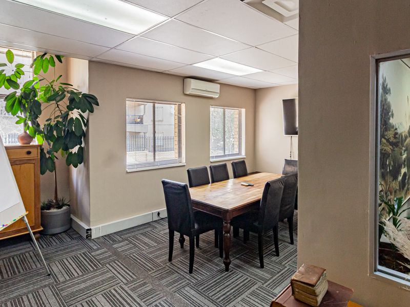 A functional office meeting room featuring carpet tiles, suspended ceiling with recessed lighting, and a wall-mounted air conditioning unit.
