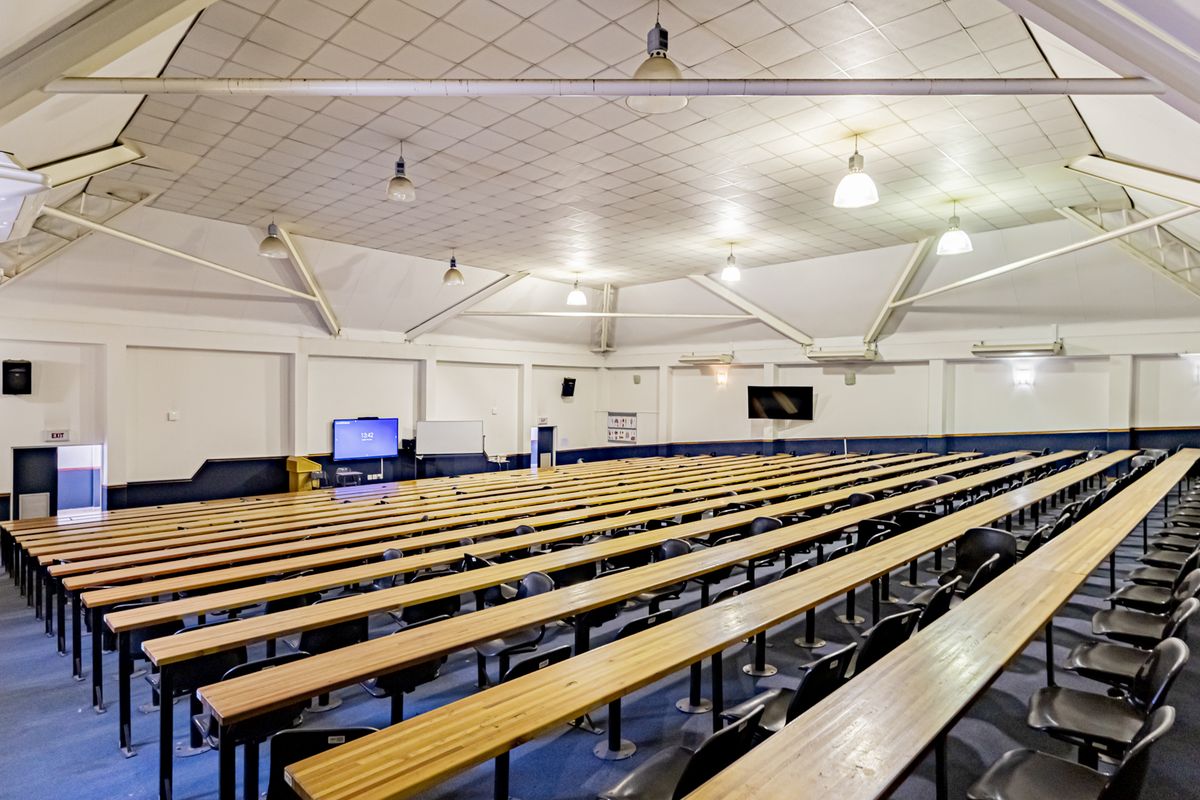 A large commercial lecture hall or conference space featuring tiered fixed bench seating, high vaulted ceilings with exposed trusses, and integrated audiovisual equipment.
