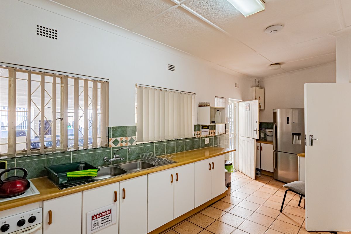 Functional kitchen featuring laminate countertops, double bowl sink, tiled splashbacks, and ample built-in cabinetry with security bars on windows.