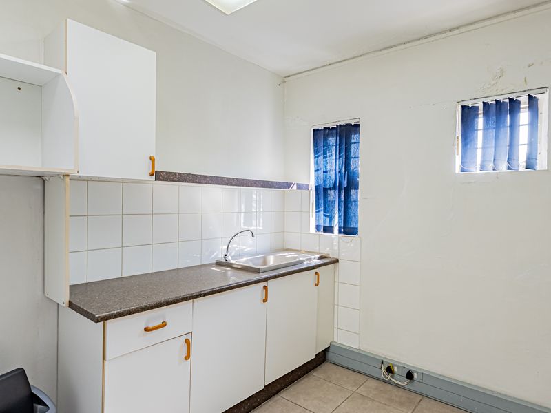 A functional scullery area featuring built-in cabinetry, a stainless steel sink, tiled splashbacks, and tiled flooring, offering a practical utility space.