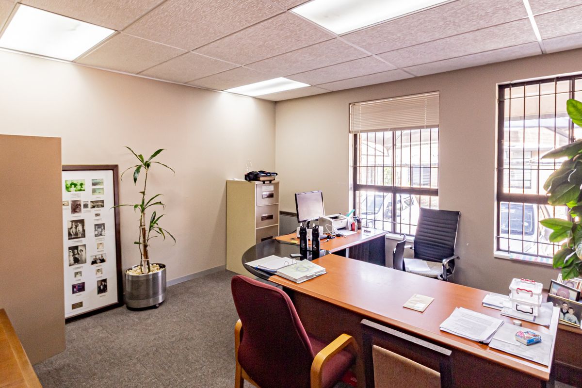 A functional office space featuring a suspended ceiling with recessed lighting, carpeted flooring, and windows fitted with security bars.