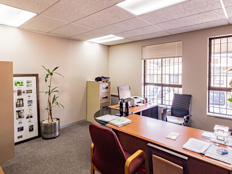 A functional office space featuring a suspended ceiling with recessed lighting, carpeted flooring, and windows fitted with security bars.