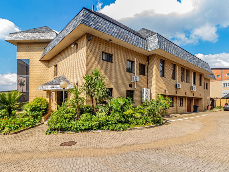 A well-maintained multi-story office building featuring a classic brick facade, slate roofing, and a paved driveway with established garden landscaping.