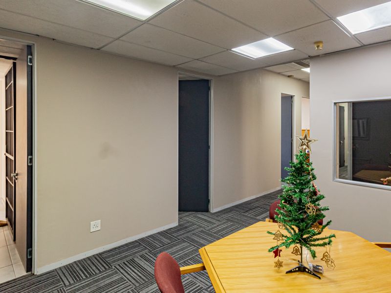 A functional office space featuring carpet tiles, a suspended ceiling with recessed lighting, and an internal glass partition providing visibility into adjacent areas.