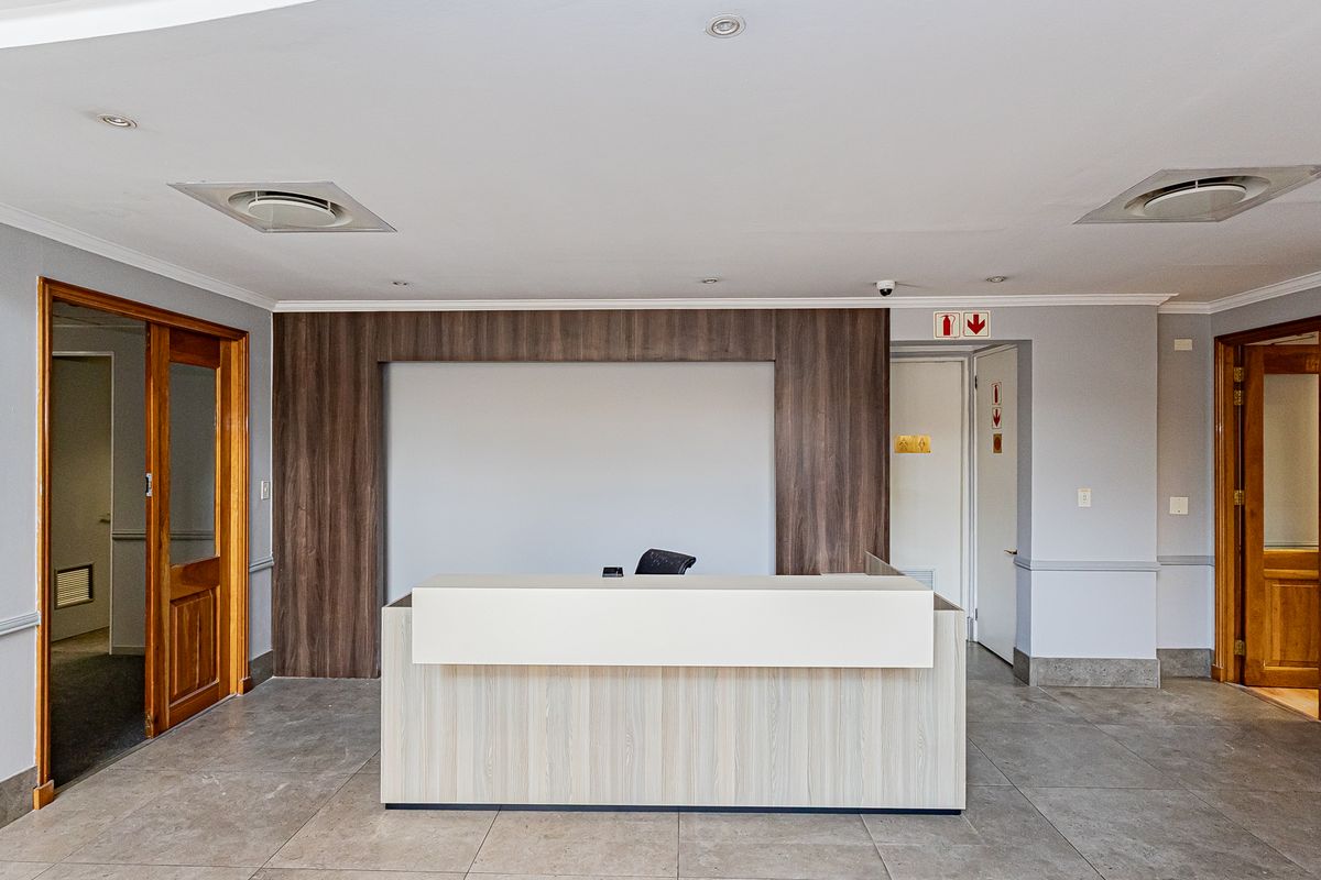 A professional office reception area featuring a built-in desk, tiled flooring, recessed lighting, and wooden door frames, providing a clean and functional workspace entrance.