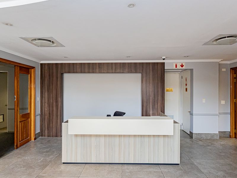 A professional office reception area featuring a built-in desk, tiled flooring, recessed lighting, and wooden door frames, providing a clean and functional workspace entrance.