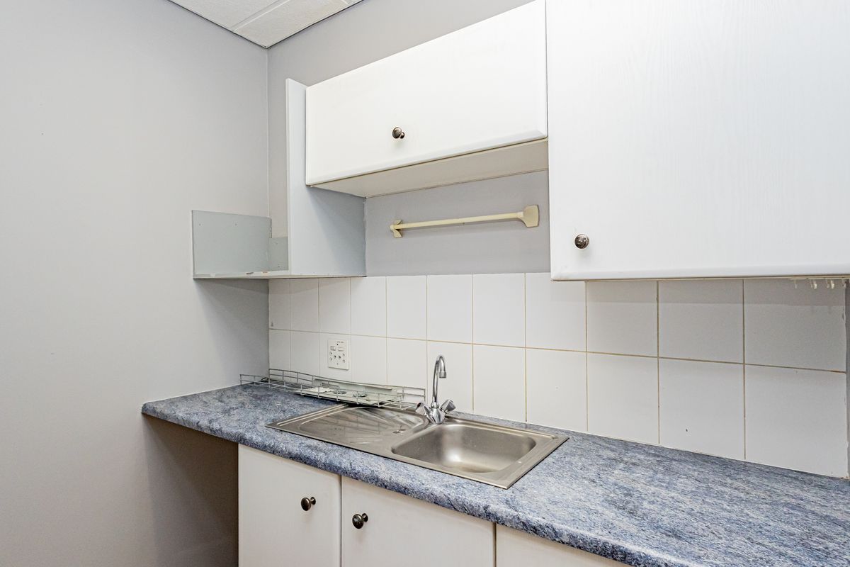 A compact office kitchenette featuring a stainless steel sink, laminate countertop, tiled backsplash, and white cabinetry for basic utility needs.