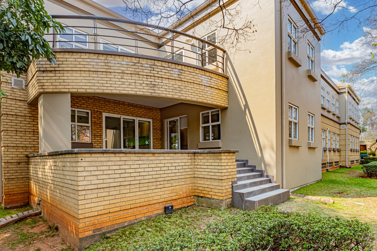 Rear exterior view of the office building featuring a brick facade, a curved balcony with metal railings, and concrete steps leading to the garden area.