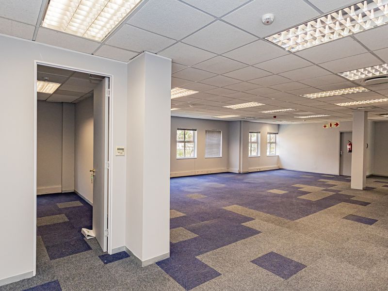 A spacious, open-plan office area featuring carpet tiles, suspended ceilings with recessed lighting, and neutral wall finishes, providing a clean and professional workspace.