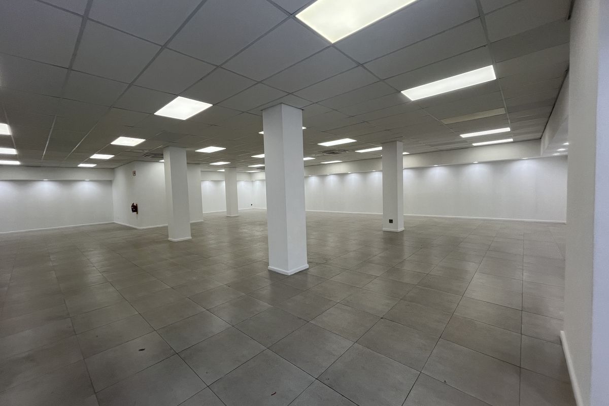 A spacious, open-plan retail area featuring neutral tiled flooring, structural support columns, and a suspended ceiling with integrated recessed lighting.